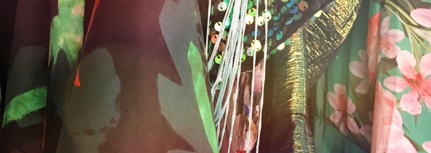 A close up of three items hanging in a wardrobe. It's unclear what the items are but two seem to be satiny, one with a Japanese inspired floral pint and the other more of an abstract bird print. The iten in the middle is a sequinned dress with long fringing.